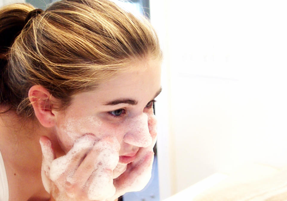 young brunette girl washing her face with lots of soap bubble details on hands.