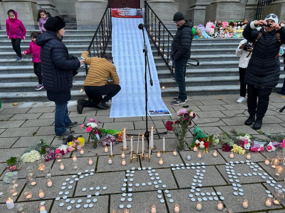 Attendees of the vigil took some time to look at the names of 10,000 Palestinians who have been killed since October 7th. The teddy bears and candles are also pictured here.  