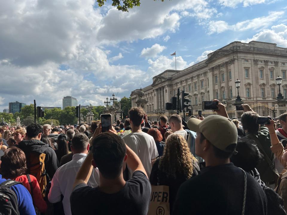 People take photos with their phones outside of Buckingham Palace.