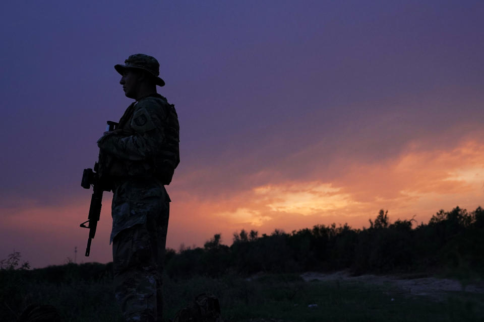 A member of the Texas Military Department stands guard along the U.S.-Mexico border Tuesday, May 11, 2021, in Roma, Texas. The U.S. government continues to report large numbers of migrants crossing the U.S.-Mexico border with an increase in adult crossers. But families and unaccompanied children are still arriving in dramatic numbers despite the weather changing in the Rio Grande Valley registering hotter days and nights. (AP Photo/Gregory Bull)