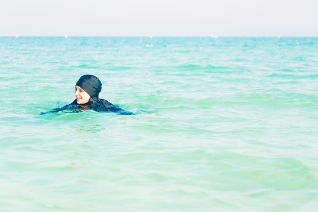 young woman in burkini swimming in the sea, persian gulf, jumeirah beach in dubai