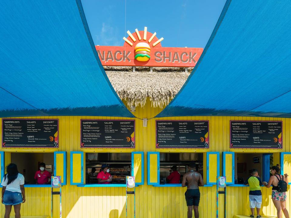 Poeple order from the Snack Shack at CocoCay with a blue awning above and clear blue skies above