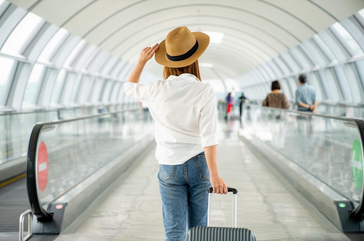 Woman in a sun hat walking through the airport pulling a suitcase