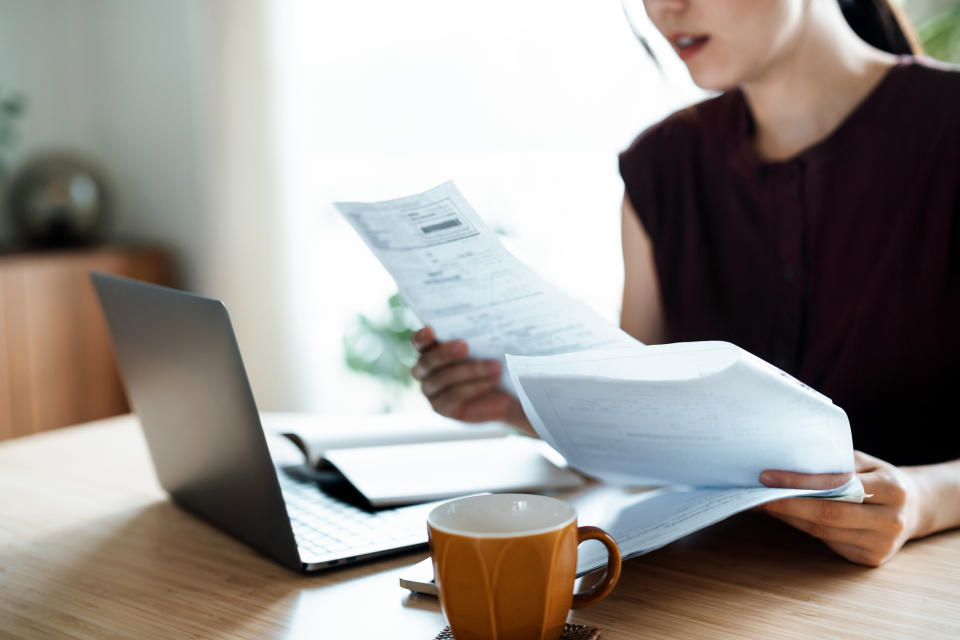 Person at a desk reviews papers while using a laptop, with a coffee cup nearby