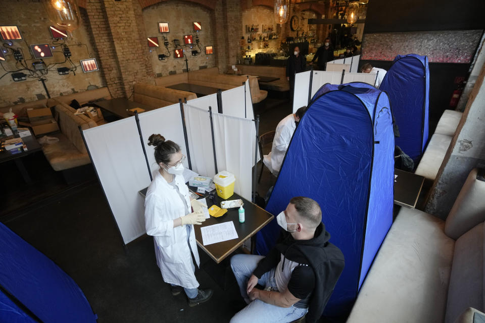 A doctor explains to a man about the side effects of the vaccination against the coronavirus and the COVID-19 disease inside the Sage Beach Bar and Restaurant in Berlin, Germany, Monday, Jan. 3, 2022. The Clubcommission Berlin, an association that protects and supports the Berlin club culture, start a vaccination campaign which take place in several clubs bars and restaurants in the German capital. (AP Photo/Markus Schreiber)