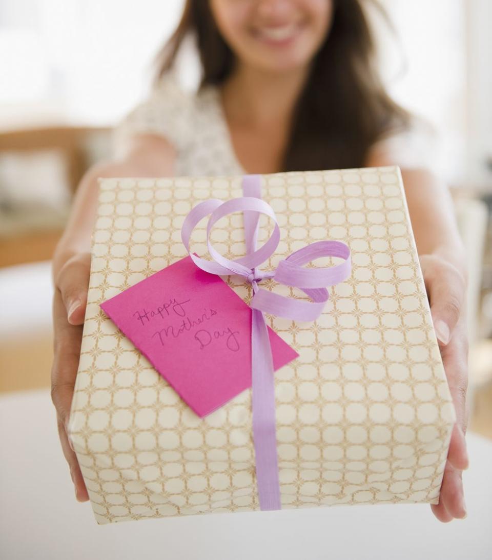 woman holding out wrapped gift box with card inscribed with the message happy mother's day