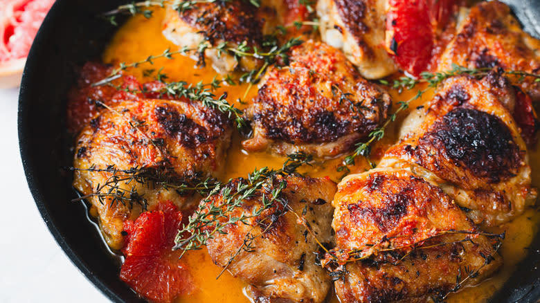 Side view of chicken in pan with grapefruit and thyme