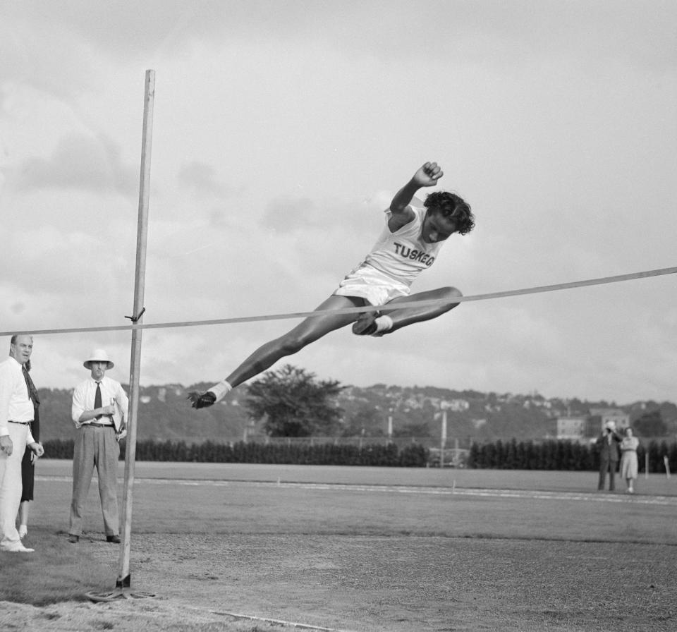 Alice Coachman leaping over a high jump bar outdoors at the National Women's Track and Field meet