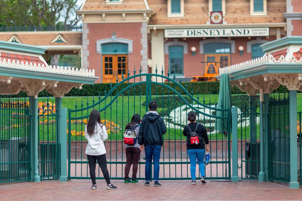 People stand outside the gates of Disneyland Park on Saturday, the first day of the closure of Disneyland and Disney California Adventure theme parks.