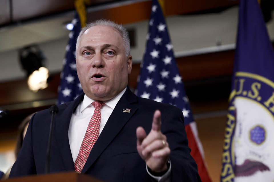 Rep. Steve Scalise raises his index finger, in front of several American flags.