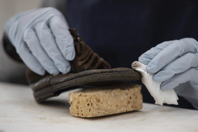 A worker rubs away dust on a shoe that belonged to a child victim of the former Nazi German death camp Auschwitz-Birkenau at the conservation laboratory on the grounds of the camp in Oswiecim, Poland, Wednesday, May 10, 2023. (AP Photo/Michal Dyjuk)