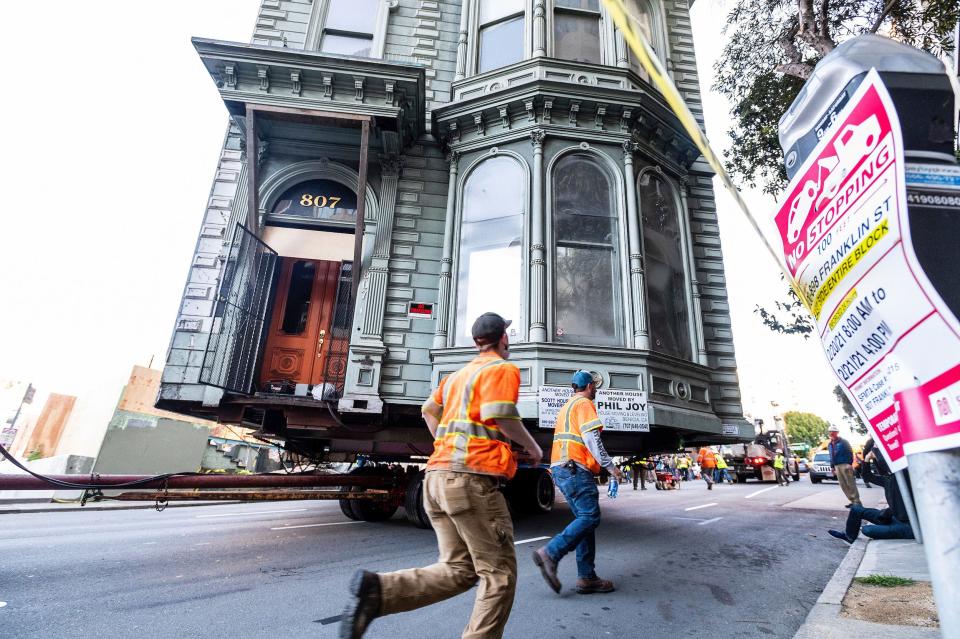 Workers pass a Victorian home as a truck pulls it through San Francisco on Sunday, Feb. 21, 2021.