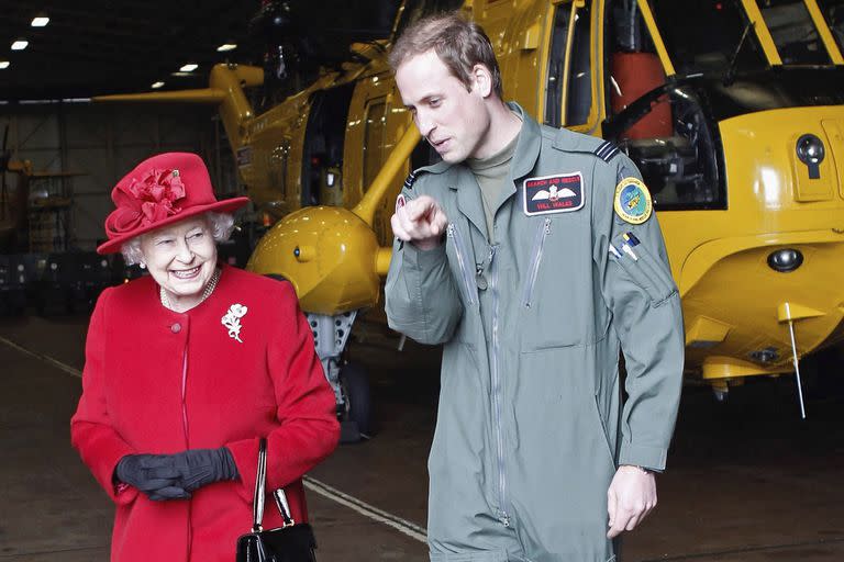 El pr&#xed;ncipe Guillermo muestra a su abuela, la reina Isabel II de Inglaterra, el hangar donde se guarda el helic&#xf3;ptero en el que realiza las pr&#xe1;cticas como piloto de b&#xfa;squeda y rescate el 1 de abril de 2011 en el cuartel de la Fuerza A&#xe9;rea brit&#xe1;nica en Holyhead, Anglesey, Reino Unido