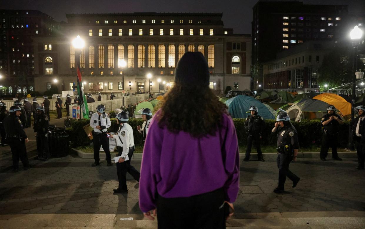 A protestor looks on as the police stand guard near an encampment of protesters supporting Palestinians on the grounds of Columbia University