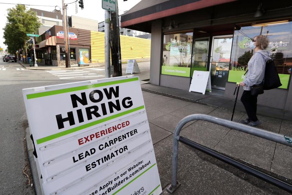 In this photo taken Thursday, June 4, 2020, a pedestrian wearing a mask walks past reader board advertising a job opening for a remodeling company, in Seattle.
