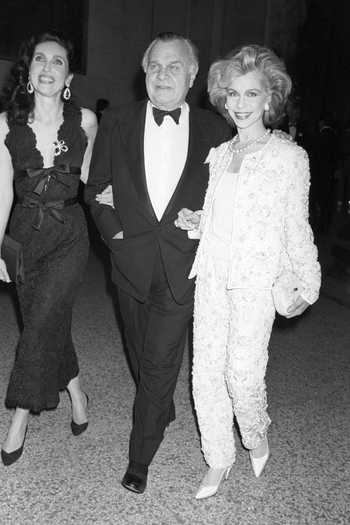 Fashion designer Bill Blass escorting his dates Veronica Hearst, wearing a black Blass dress and Lynn Wyatt wearing a creamy-yellow Blass pantsuit to the Metropolitan Museum of Art's annual gala fund-raiser benefiting the Costume Institute where the museums restaurant was turned into an ooh-la-la replica of a Paris bistro of the Fifties, by John Funt with slides of Paris by night projected on the walls and the whole place lighted in pink on December 8, 1992 in New York..Article title: 'Eye: A Gala Night for the Met, A New Look for the Costume Institute.