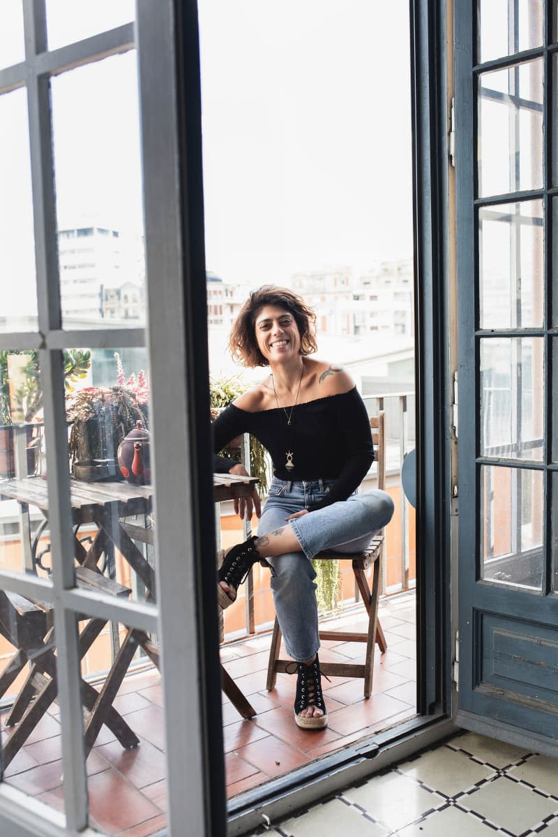 Dweller sits at wood cafe table with plants on outdoor balcony.