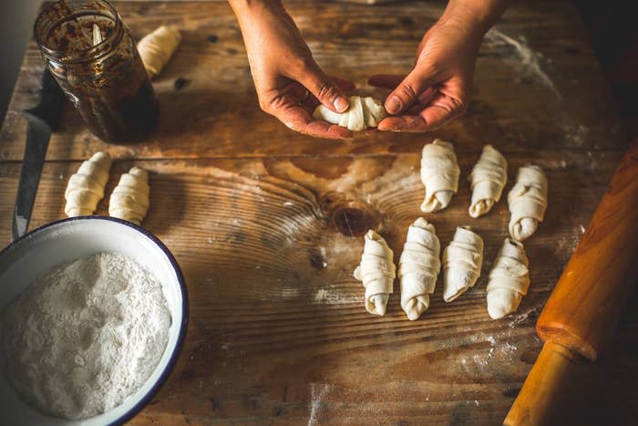 A person rolling croissants from dough.