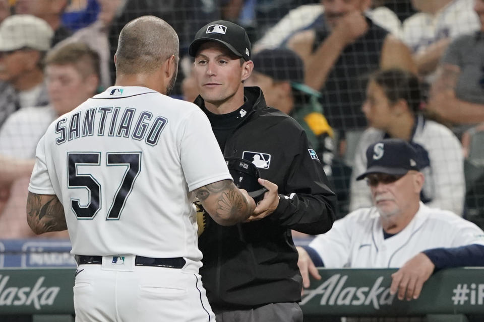 Seattle Mariners pitcher Hector Santiago has his cap checked for foreign substances by an umpire after the top of the fifth inning of the team's baseball game against the Houston Astros, Tuesday, July 27, 2021, in Seattle. It was the first game back for Santiago after he served a 10-game suspension for violating MLB's rules for foreign substances that could aid in pitching. (AP Photo/Ted S. Warren)