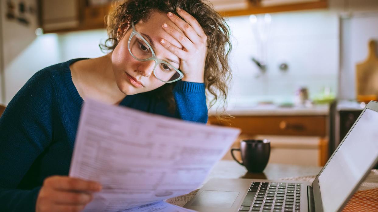 Young brunette curly female reading her bill papers, looking stressed.