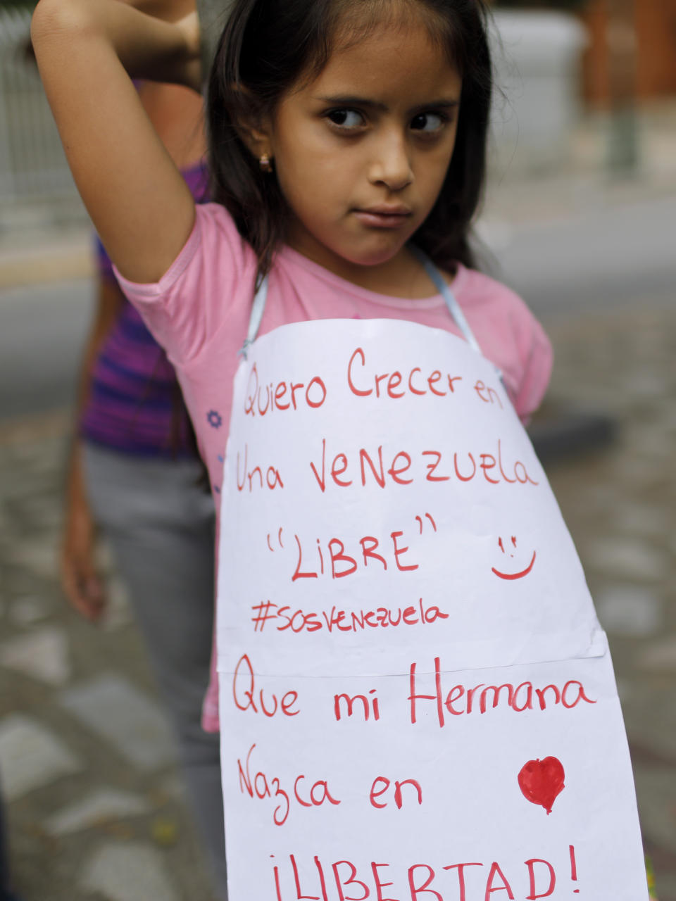 A girl wears an apron reading in Spanish "I want to grow up in a free Venezuela and that my sister will born in freedom" during a march of opponents to Venezuela's President Nicolas Maduro in Caracas, Venezuela, Saturday, May 4, 2019. Opposition leader Juan Guaido took his quest to win over Venezuela's troops back to the streets calling his supporters to participate in a mobilization outside military installations around the country. (AP Photo/Ariana Cubillos)