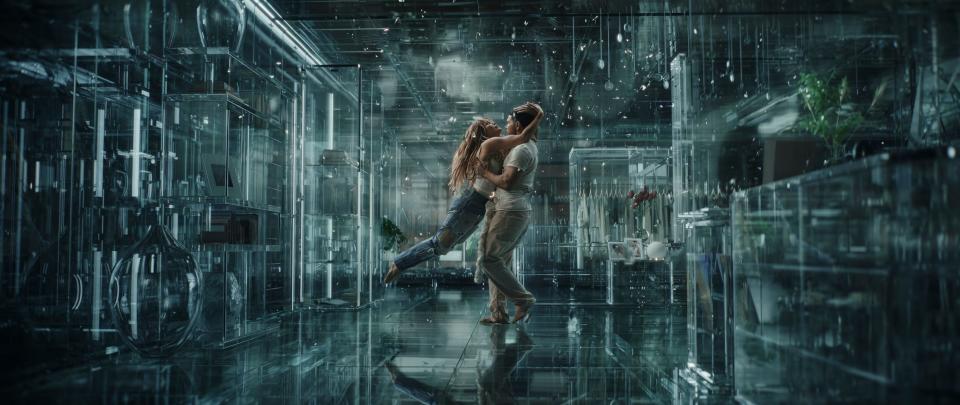 jennifer lopez embraces a man in a blue space that looks like a tech simulation of a nice bedroom