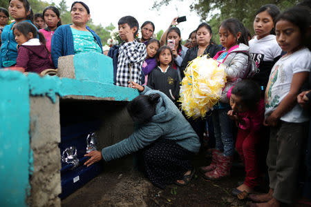 A woman reaches into the grave to touch the casket of Misael Paiz, 25, at his funeral in Aguacate, Huehuetenango, Guatemala, October 29, 2018. REUTERS/Lucy Nicholson