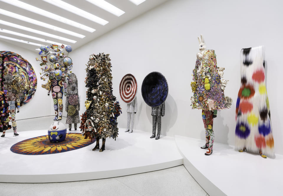 Installation view, Nick Cave: Forothermore, Solomon R. Guggenheim Museum, November 18, 2022–April 10, 2023. © Solomon R. Guggenheim Foundation, New York. Photo: Ariel Ione Williams. Shows a series of "Soundsuits" as they are on display in the exhibit. All walls and floor are stark white providing ideal contrast with the colorful art pieces.