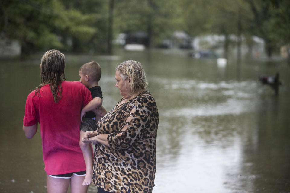 Tiffany Loden, left, holds her son, Braxton, as she and Linda Anson stand at the edge of their flooded neighborhood inundated by rains from Tropical Depression Imelda on Thursday, Sept. 19, 2019, in Spendora. Her house, where she has lived for just two weeks, is the one with the white roof. (Brett Coomer/Houston Chronicle via AP)