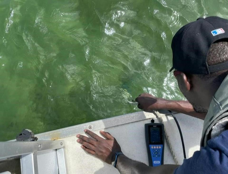 A man leans over the edge of a boat holding a rope attached to sampling devices in the water below.