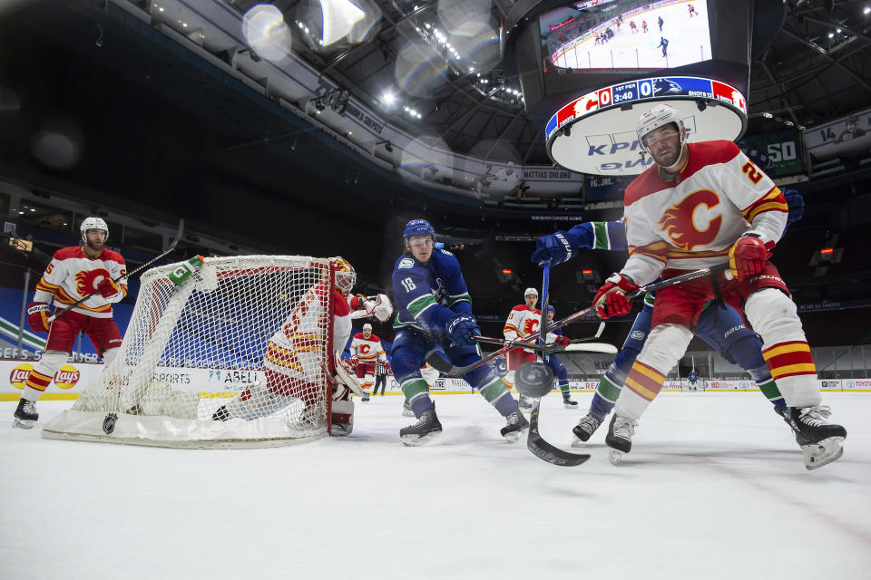 Vancouver Canucks' Jake Virtanen (18) and Calgary Flames' Josh Leivo (27) vie for the puck as goalie Jacob Markstrom watches during the first period of an NHL hockey game Saturday, Feb. 13, 2021, in Vancouver, British Columbia. (Darryl Dyck/The Canadian Press via AP)