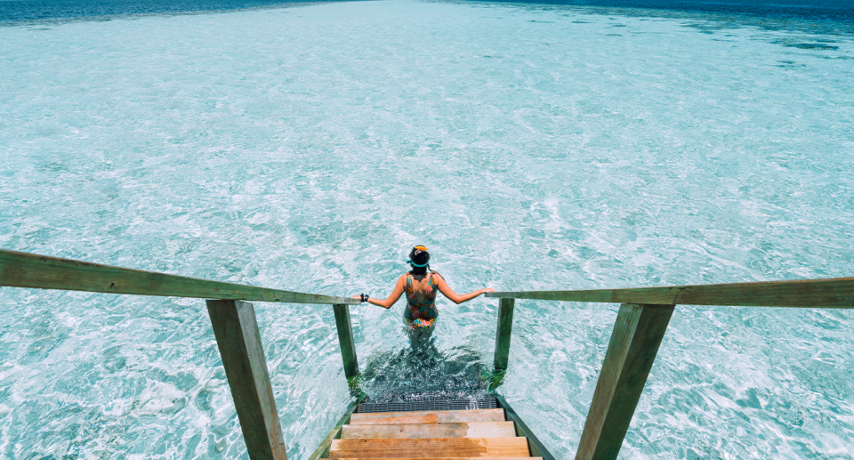 A woman walking down stairs into the sea at at Maldives resort. 