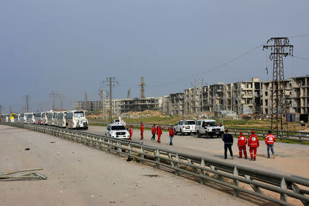 Syrian Arab Red Crescent members stand near a convoy of buses carrying evacuees from the two Shi'ite villages of al-Foua and Kefraya, upon their arrival in government-controlled Aleppo, in this handout picture provided by SANA on April 12, 2017. SANA/Handout via REUTERS