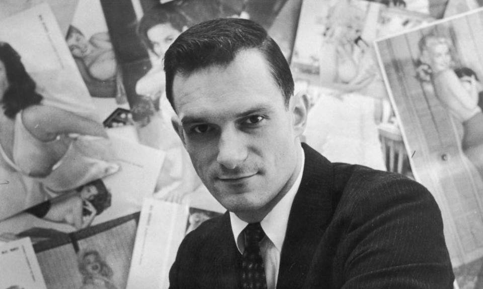 Portrait of American publisher Hugh Hefner sitting in front of a wall collage of female centerfolds from his men’s magazine ‘Playboy’