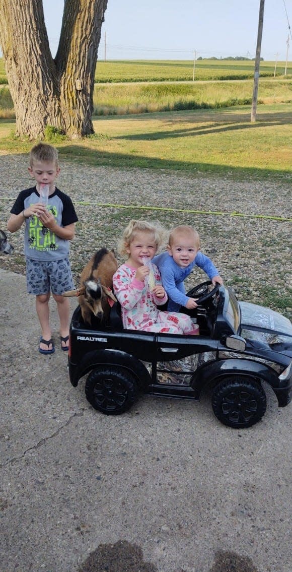 Hunter (left) standing behind Oaklee (center) and Walker driving a toy car.