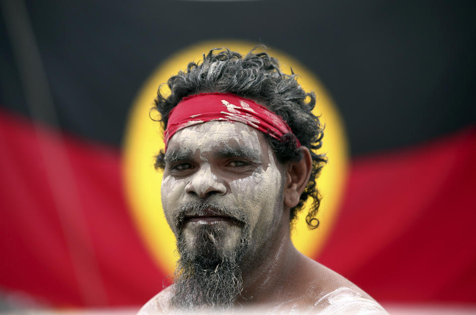 FILE - Stedman Sailor stands in front of the Aboriginal Australian Flag as he arrives with other members of the Aboriginal community to take part in a smoking ceremony as part of Australia Day celebrations in Sydney, Jan. 26, 2018. Australia’s House of Representatives voted overwhelming on Wednesday, May 31, 2023 in favor of holding a referendum this year on creating a so-called Indigenous Voice to Parliament, an advocate that promises the nation’s most disadvantaged ethnic minority more say on policies that effect their lives. (AP Photo/Rick Rycroft, File)