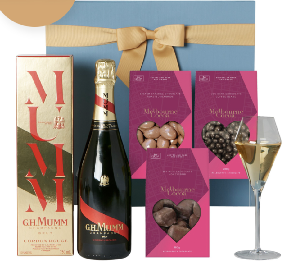 The Gourmet Pantry G.H.Mumm Champagne & Premium Chocolate Hamper, showing chocolates in pink packaging with love heart cutouts, and a bottle of GH Mumm Champagne next to its gold and red box.