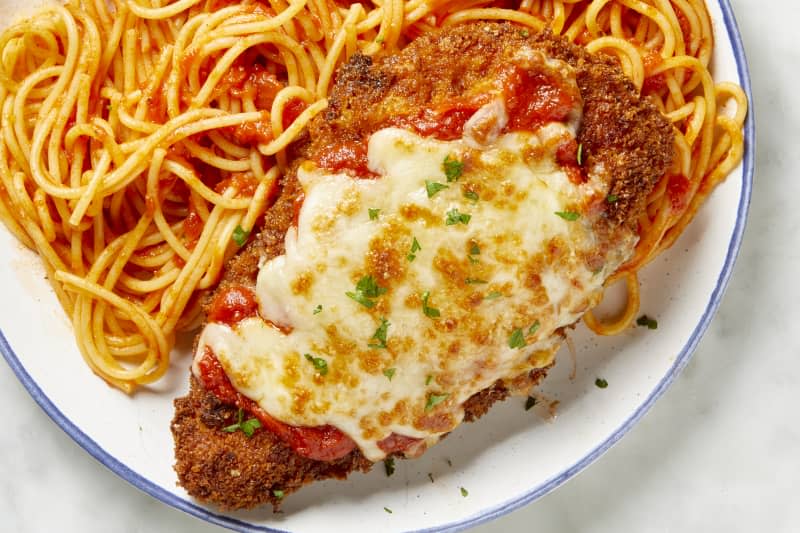 Overhead view of chicken parmesan over spaghetti on a white plate with a blue outer rim.