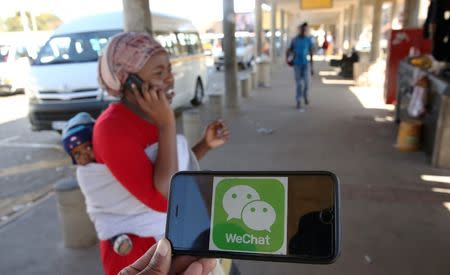 A WeChat logo is displayed on a mobile phone as a woman walks past as she talks on her mobile phone at a taxi rank in this picture illustration taken July 21, 2016. Picture taken July 21, 2016. REUTERS/Siphiwe Sibeko/Illustration