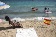 A Spanish flag being used as social distancing signage sticks out from the sand in Palma de Mallorca, Spain, Sunday, July 26, 2020. Britain has put Spain back on its unsafe list and announced Saturday that travelers arriving in the U.K. from Spain must now quarantine for 14 days. The move by the UK taken without forewarning has caught travelers off guard. (AP Photo/Joan Mateu)