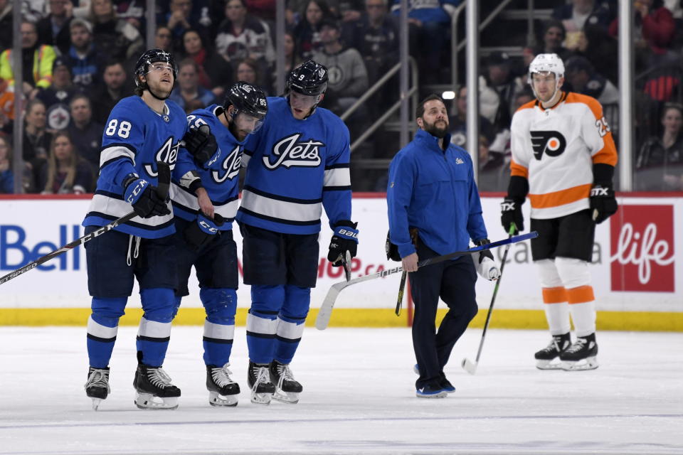 Winnipeg Jets' Mathieu Perreault (85) is helped off the ice by teammates Nathan Beaulieu (88) and Andrew Copp (9) after being injured during second-period NHL hockey game action against the Philadelphia Flyers in Winnipeg, Manitoba, Sunday, Dec. 15, 2019. (Fred Greenslade/The Canadian Press via AP)