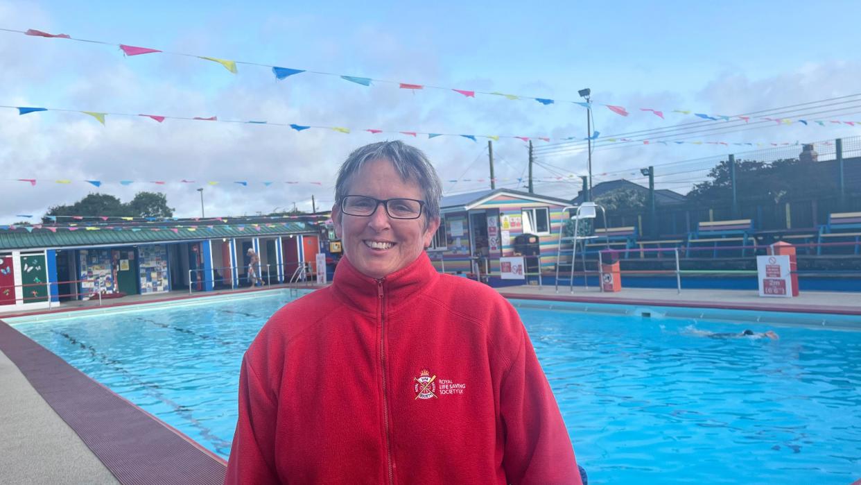 Steff Wells, wearing a red fleece and glasses, standing beside the pool