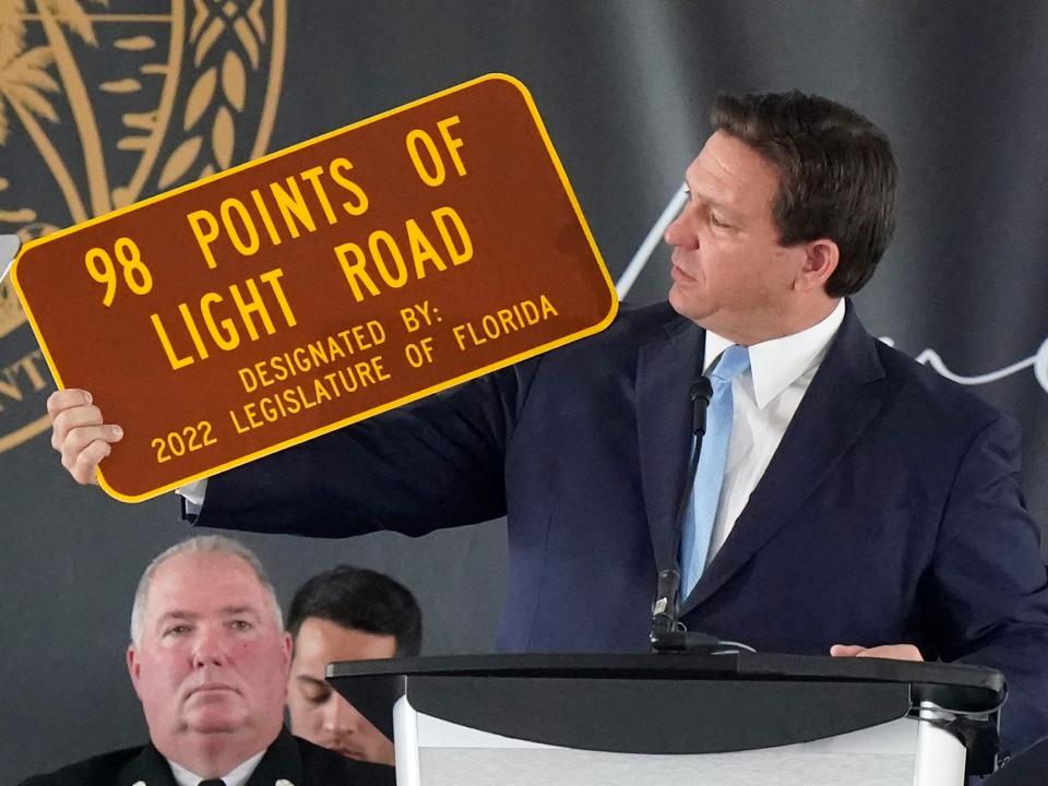 Florida Gov. Ron DeSantis holds up a sign dedicated to the 98 people who lost their lives during a remembrance event at the site of the Champlain Towers South building collapse, Friday, June 24, 2022, in Surfside, Florida.