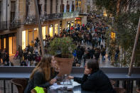 FILE - In this Dec. 7, 2020, file photo, a couple sit on a bar terrace as people wearing face masks to protect against the spread of coronavirus walk along a street in downtown Barcelona, Spain. While most of Europe kicked off 2021 with earlier curfews or stay-at-home orders, authorities in Spain insist the new coronavirus variant causing havoc elsewhere is not to blame for a sharp resurgence of cases and that the country can avoid a full lockdown even as its hospitals fill up. (AP Photo/Emilio Morenatti, File)