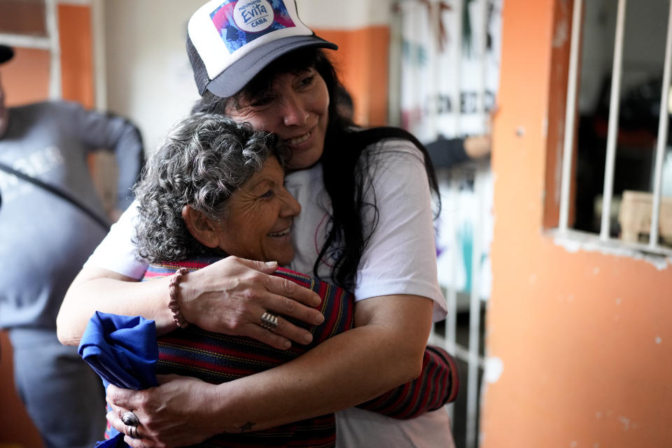 Maria Eva Noble, member of the social movement "Movimiento Evita," or Evita Movement, wearing hat, hugs a fellow volunteer at a soup kitchen in Buenos Aires, Argentina, Tuesday, July 26, 2022, the day of the 70th anniversary of the death of Argentina's most famous first lady, who died of cancer on July 26, 1952 at the age of 33. Noble was named after Argentina's late first lady, Maria Eva Duarte de Peron, better known as Evita. (AP Photo/Natacha Pisarenko)