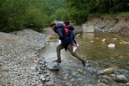 A man carrying a child who tried to cross the Greek-Macedonian border crosses a small river on their way back to a makeshift camp for refugees and migrants at the border near the village of Idomeni, Greece, May 12, 2016. REUTERS/Marko Djurica