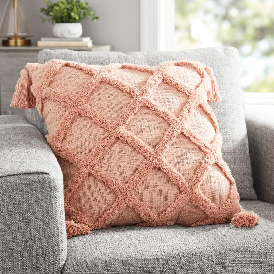 The coral pillow with a tufted trellis pattern resting on a chair