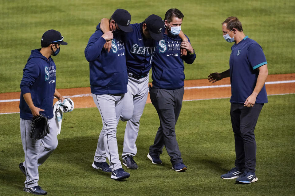 Seattle Mariners starting pitcher Yusei Kikuchi, center, is helped off the field after being hit by a ball hit by Los Angeles Angels' David Fletcher during the fifth inning of a baseball game Saturday, June 5, 2021, in Anaheim, Calif. (AP Photo/Ashley Landis)