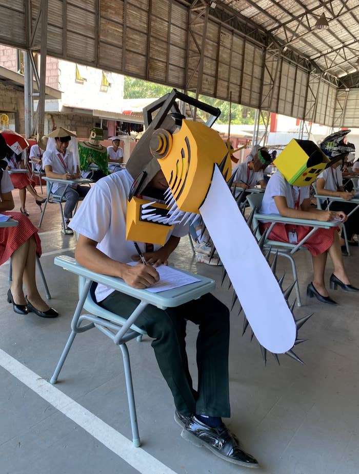 Person in a classroom wearing a large chainsaw hat while writing on a paper