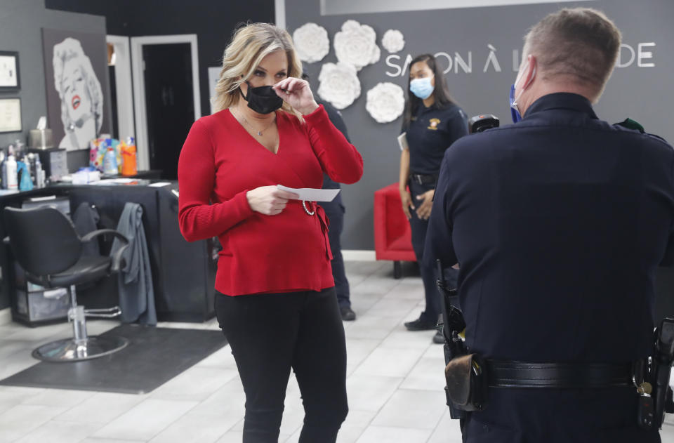 Salon owner Shelley Luther holds a citation and speaks with a Dallas police officer after she was cited for reopening her Salon A la Mode in Dallas, Friday, April 24, 2020. Hair salons have not been cleared for reopening in Texas. Luther was asked by officials to close and was issued a citation when she refused. Luther said she will remain open for business. (AP Photo/LM Otero)